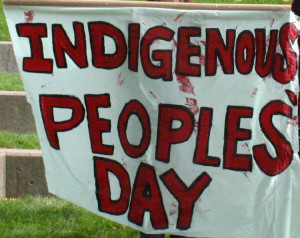 Hand-painted banner, waving slightly in wind, red letters on white background, saying "Indigenous People's Day"